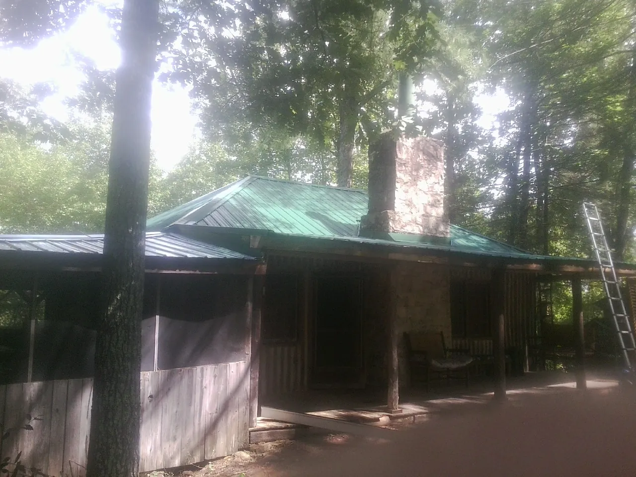 Green metal roof and stone chimney above a log cabin porch in Edinburg